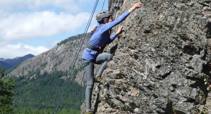 a student scales a rock wall on an outward bound trip for teens